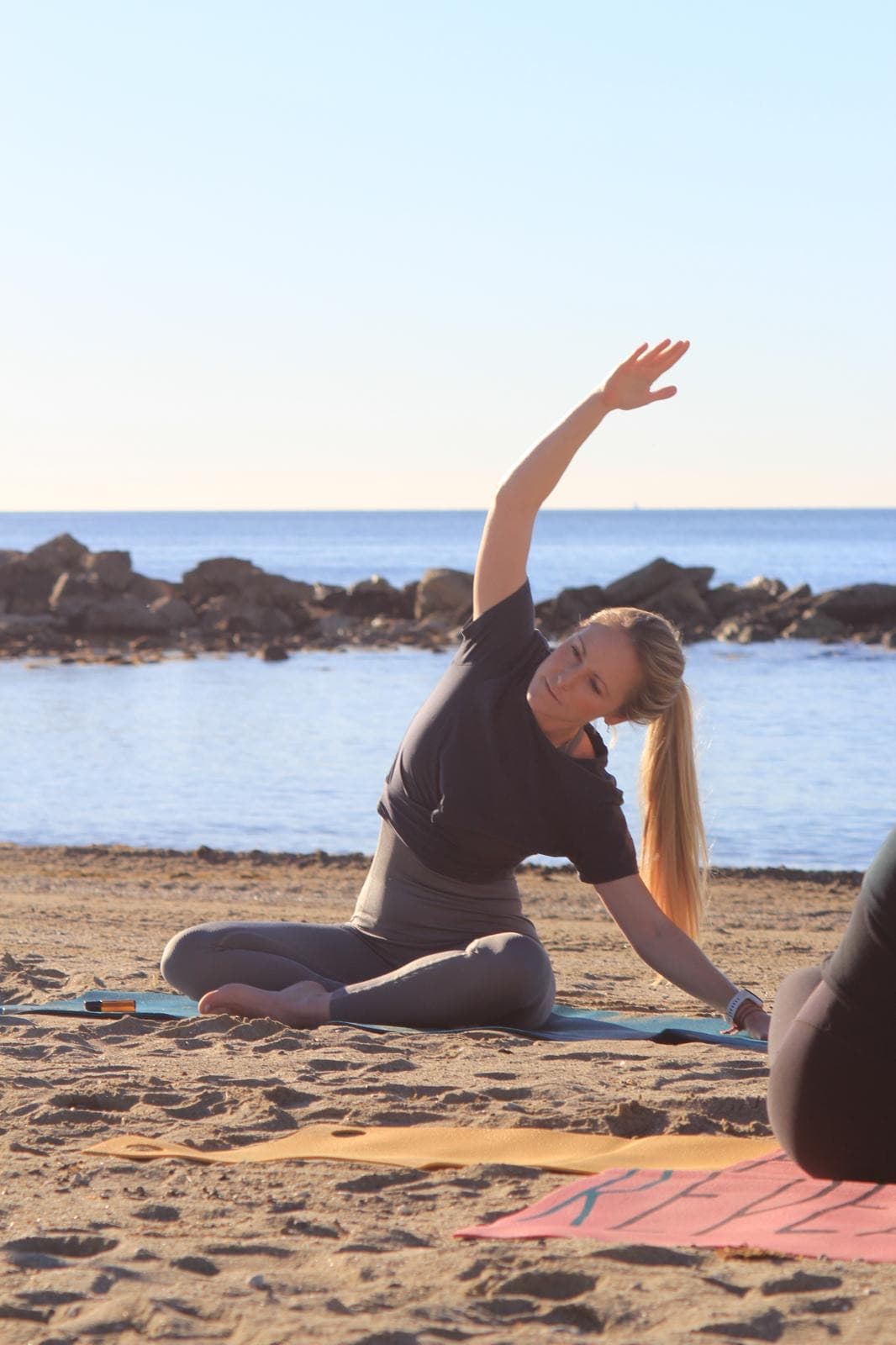 Skye in a seated side-stretch on the beach
