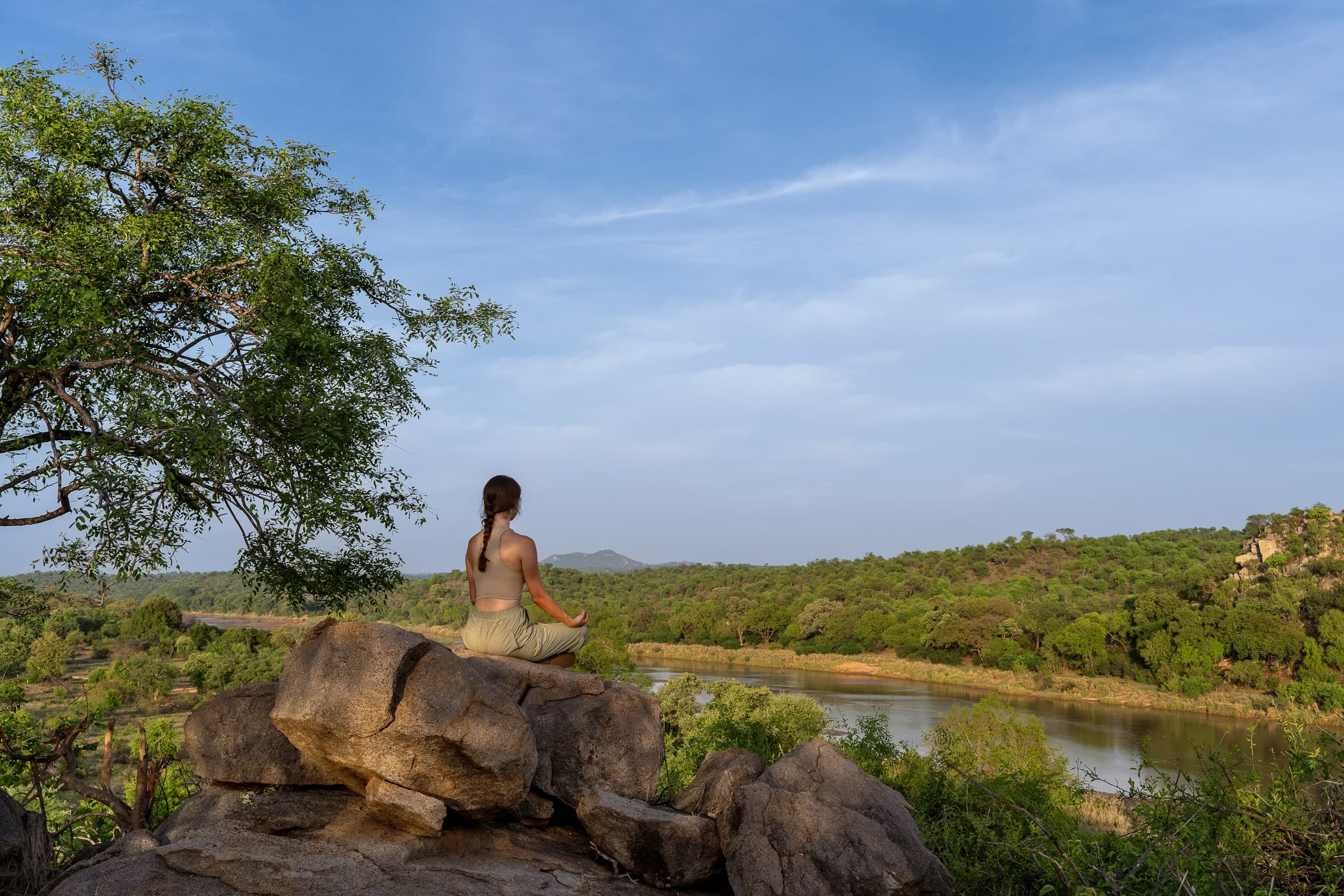 A guest meditating on the rocks above the Sashwa river under a bright blue sky